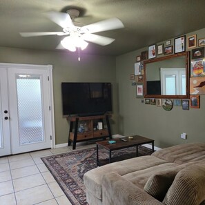 A living room with a ceiling fan, a television on a wooden stand, a coffee table, a sofa, and a patterned rug. - Pet-Friendly Townhome w/ Fire Pit, 5mins to Beach (Fort Walton Beach)