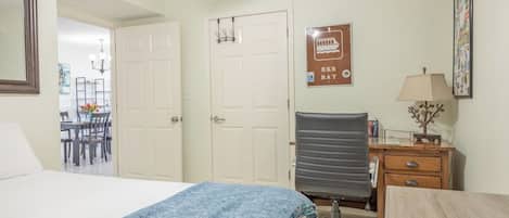 Een hotelkamer met een bed, een bureau, een stoel, en een eethoek zichtbaar door een open deur.