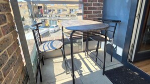 A balcony with a table and chairs, a brick wall, and a view of buildings. - Cozy City 1Br W/balcony at the Heart of Stratford (London)