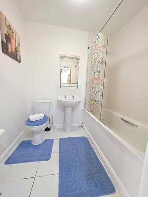 Ein Badezimmer mit Toilette, Waschbecken und Dusche. Blaue Matten liegen auf dem Boden.