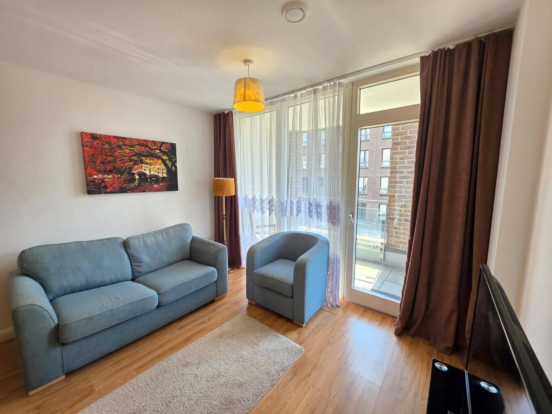 A living room with a sofa, armchair, and a painting on the wall.