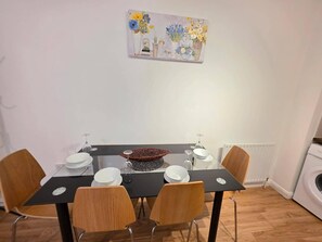 A dining area with a glass table, wooden chairs, and a painting above. - Cozy City 1Br W/balcony at the Heart of Stratford (London)