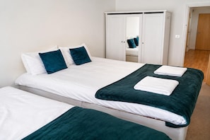 A double bed with white bedding and teal pillows, a wardrobe with a mirror, and a wooden floor. - Cozy City 1Br W/balcony at the Heart of Stratford (London)