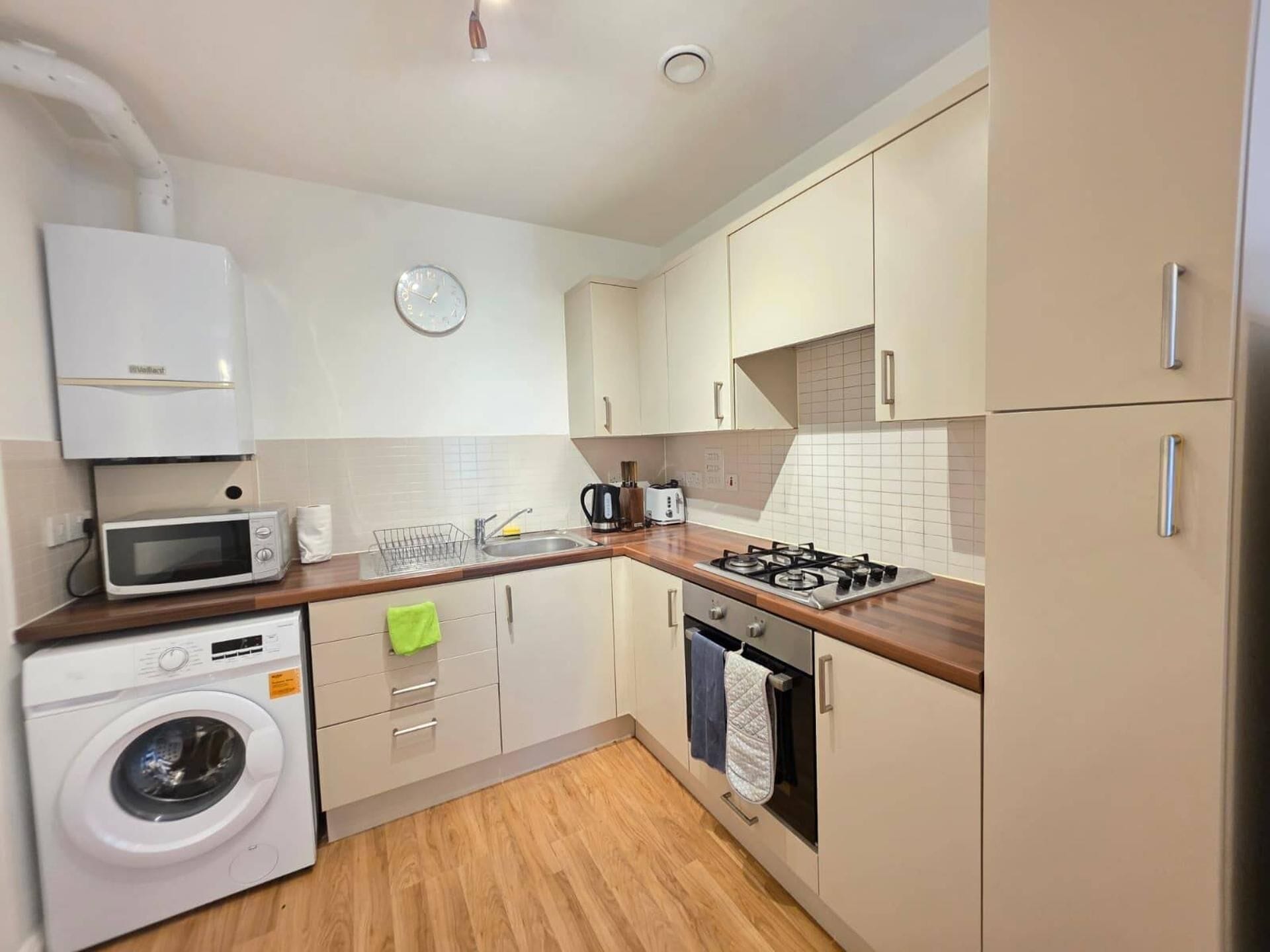 A compact kitchen with a washing machine, microwave, sink, and stove.