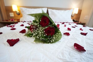 Ein Bett mit einem Strauß roter Rosen und verstreuten Rosenblättern.