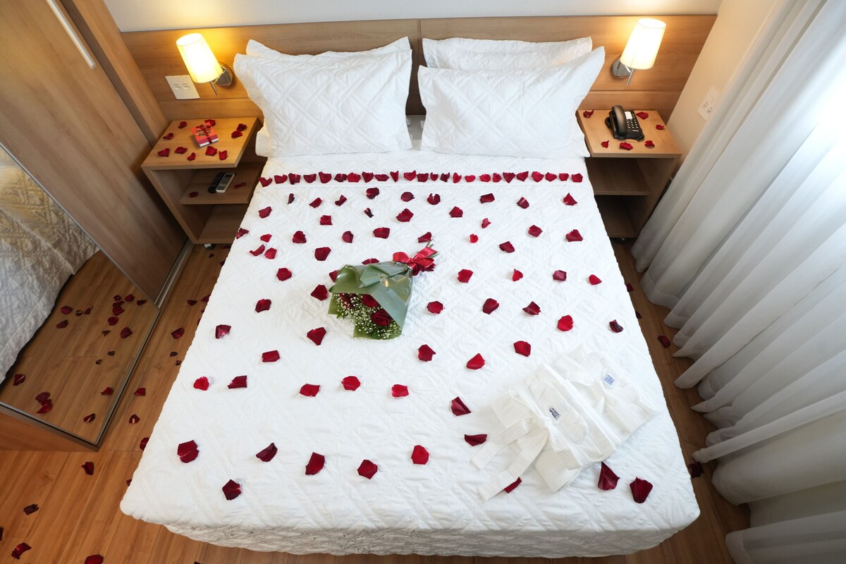 Ein Hotelzimmer mit einem Bett, zwei Nachttischen, einer Lampe und einem Blumenstrauß.