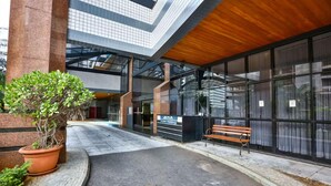 Entrada de un edificio moderno con un banco, un letrero que dice 'Hotel Parking' y una planta en maceta.