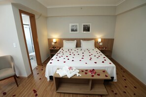 Ein Hotelzimmer mit einem großen Bett, zwei Nachttischen, einem Holzboden, einem Stuhl und einer Tür zu einem Badezimmer.