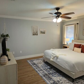 Ein Schlafzimmer mit einem Bett, einem Deckenventilator, einem Nachttisch, einer Lampe und einer an der Wand befestigten Pflanze.