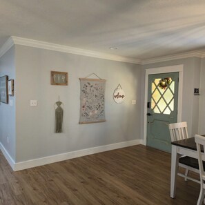 Une pièce dotée d’un plancher en bois, d’une porte blanche avec un panneau en verre dépoli et de décorations murales, notamment un panneau d’accueil et des œuvres d’art encadrées.
