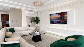 Una sala moderna con un sofá seccional, un sillón verde, una mesa de centro, un televisor de pantalla plana montado en la pared y un ventilador de techo.