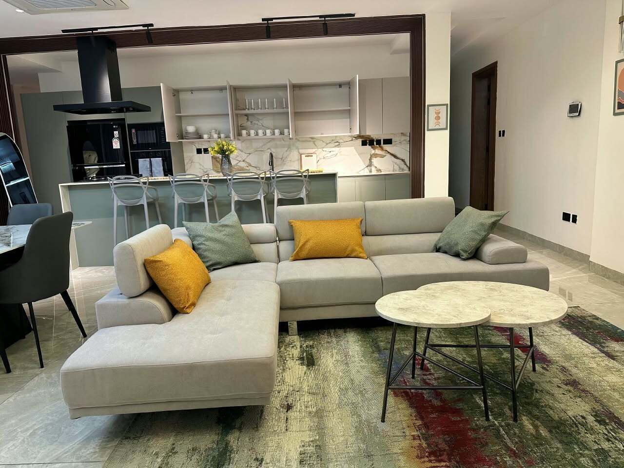 Una sala moderna con un sofá modular, una mesa de comedor y una cocina al fondo.