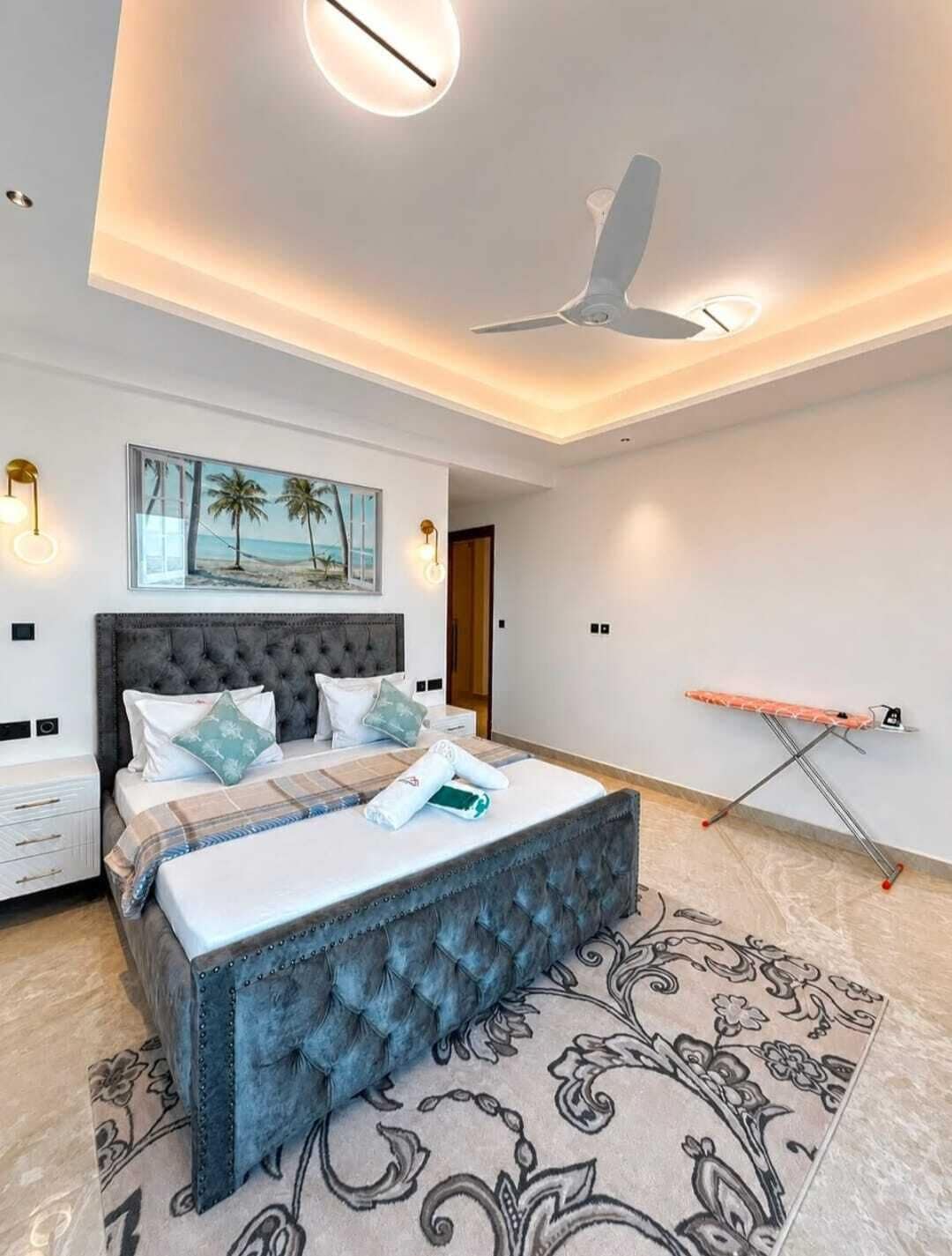 A modern bedroom with a tufted headboard, a flat-screen TV, and a ceiling fan.
