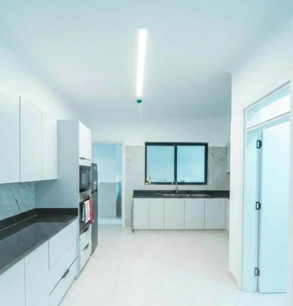A modern kitchen with white cabinets, a black countertop, a built-in oven, and a window above the sink.