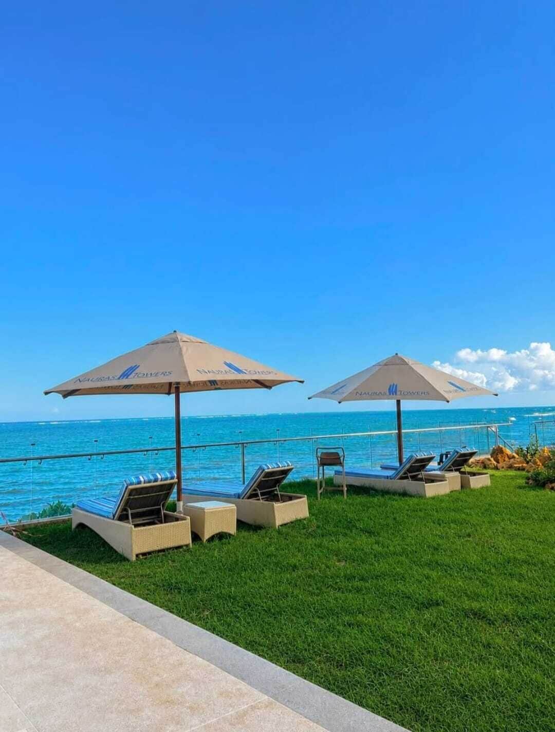 A poolside area with lounge chairs and umbrellas, overlooking a clear blue ocean.