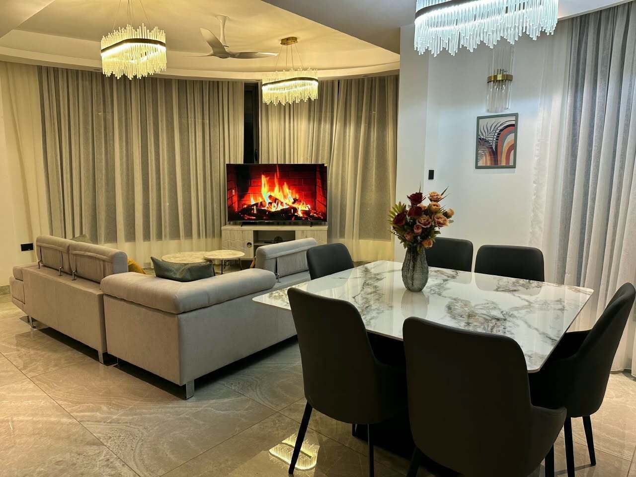 A modern living room with a sofa set, a dining table with chairs, a fireplace, and a television.