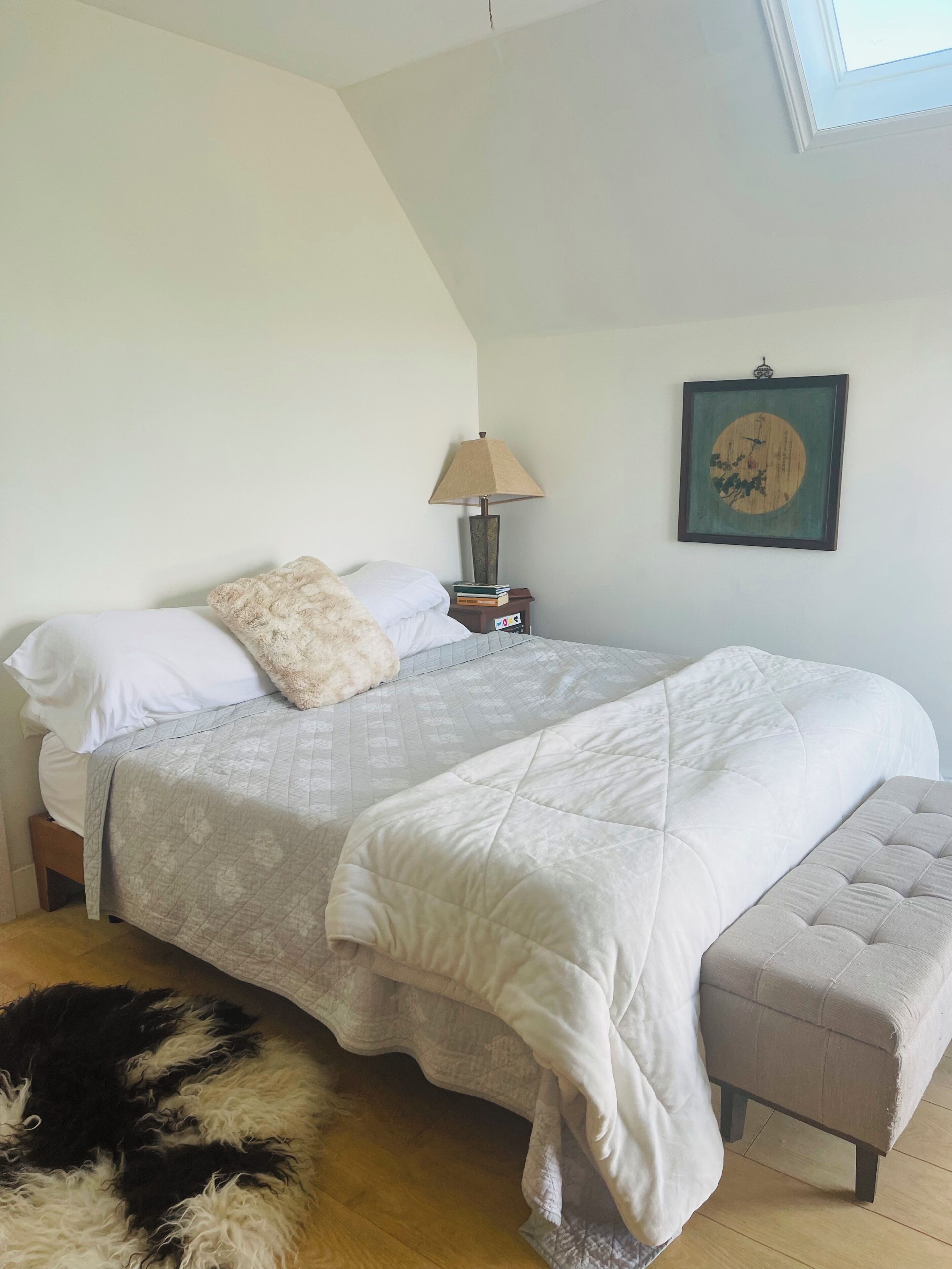 A bedroom with a bed, bedside table, lamp, and a framed picture on the wall.