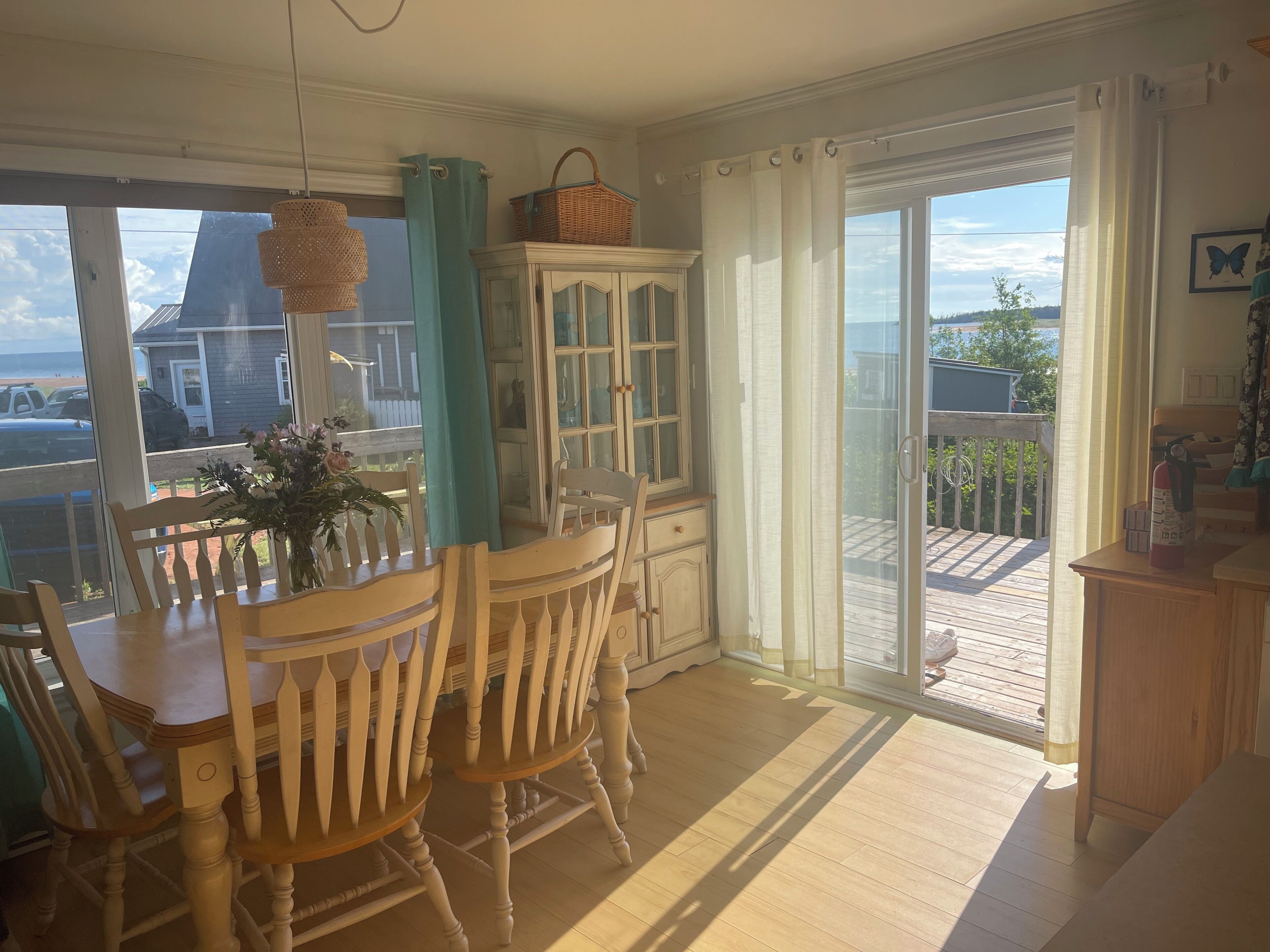 A dining area with a wooden table and chairs, a cabinet with glass doors, and a view through a sliding glass door to an outdoor deck.