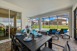 An outdoor patio with a dining table set for four, surrounded by chairs, and a pool area visible in the background. - Brand New   6BR Villa Pool   Spa  PS5 Loft 2380 (Kissimmee)