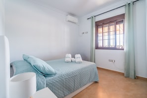 A hotel room with a bed, a window with curtains, an air conditioning unit, and a wall socket. - Cubo's Casa San Francisco & Private Pool / air conditioning / BBQ / free wifi (Málaga)