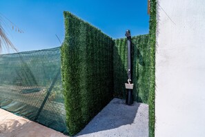 Ein Weg, der an einer grünen Hecke und einer weißen Mauer entlangführt und zu einem schwarzen Pfosten mit einer Ampel führt.