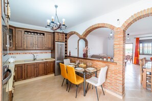 Une cuisine avec des meubles en bois, un réfrigérateur en acier inoxydable et un coin repas avec des chaises jaunes et une table en verre.