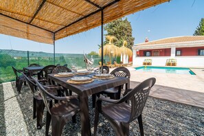 Un espace extérieur aménagé pour les repas, avec une table dressée, entourée de chaises, et une piscine en arrière-plan.
