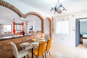 A dining area with a brick partition, yellow chairs, and a glass table. - Cubo's Casa San Francisco & Private Pool / air conditioning / BBQ / free wifi (Málaga)