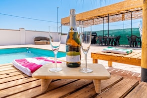 A wooden table with a bottle of Brutino wine and two glasses, a pool, and outdoor seating. - Cubo's Casa San Francisco & Private Pool / air conditioning / BBQ / free wifi (Málaga)