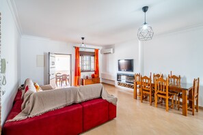 A living room with a red sofa, wooden dining table, and chairs, a TV, and a ceiling light fixture. - Cubo's Casa San Francisco & Private Pool / air conditioning / BBQ / free wifi (Málaga)