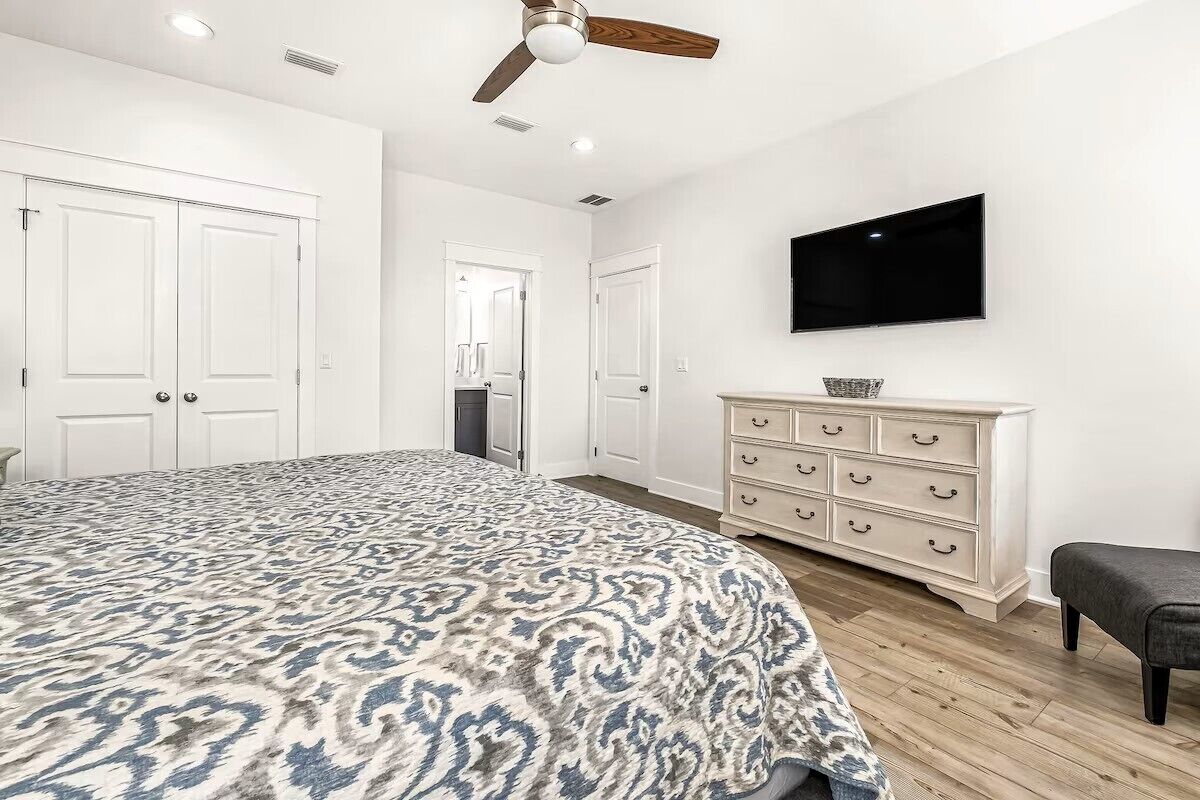A bedroom with a bed, a dresser, a television, and a ceiling fan.