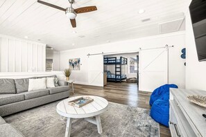 Un salon spacieux avec un canapé gris, une table basse ronde et un pouf bleu.