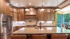 Une cuisine moderne avec des meubles en bois, des appareils en acier inoxydable, un grand îlot central doté de tabourets et un éclairage suspendu.