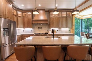 Een moderne keuken met houten kasten, roestvrijstalen apparatuur, een groot eiland met barkrukken en hanglampen.