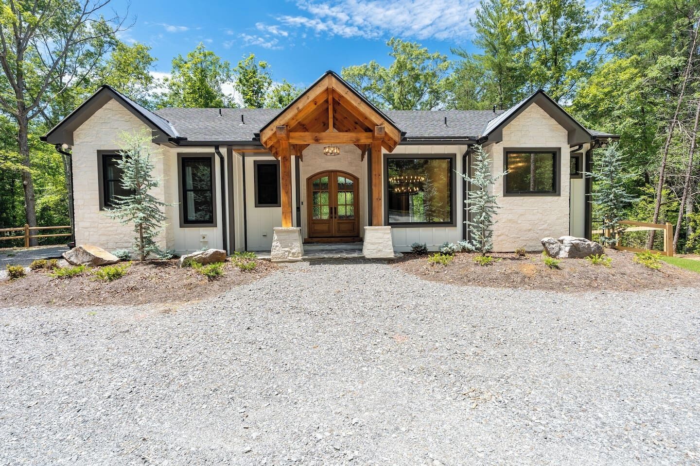 A modern two-story house with a stone facade, a wooden porch, and a gravel driveway.