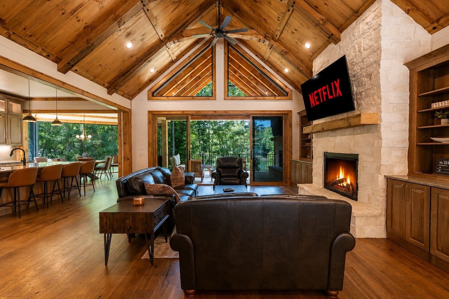 A spacious living area with a fireplace, a large TV screen displaying 'NETFLIX', and a view of the outdoors through large windows.