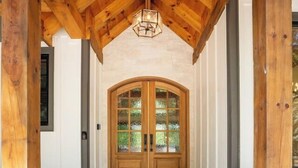 Une véranda en bois dotée d’un sol en pierre menant à une porte en bois avec des panneaux de verre.
