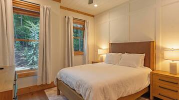 A bedroom with a large bed, two bedside tables, a ceiling fan, and windows with curtains.