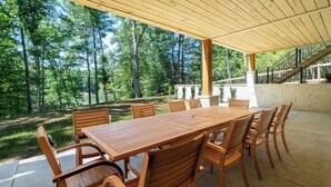Une terrasse extérieure avec une table et des chaises en bois, entourée d’un mur de pierre et offrant une vue sur une zone boisée.