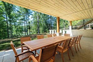 Een terras buiten met een houten tafel en stoelen, omgeven door een stenen muur en uitzicht op een bebost gebied.
