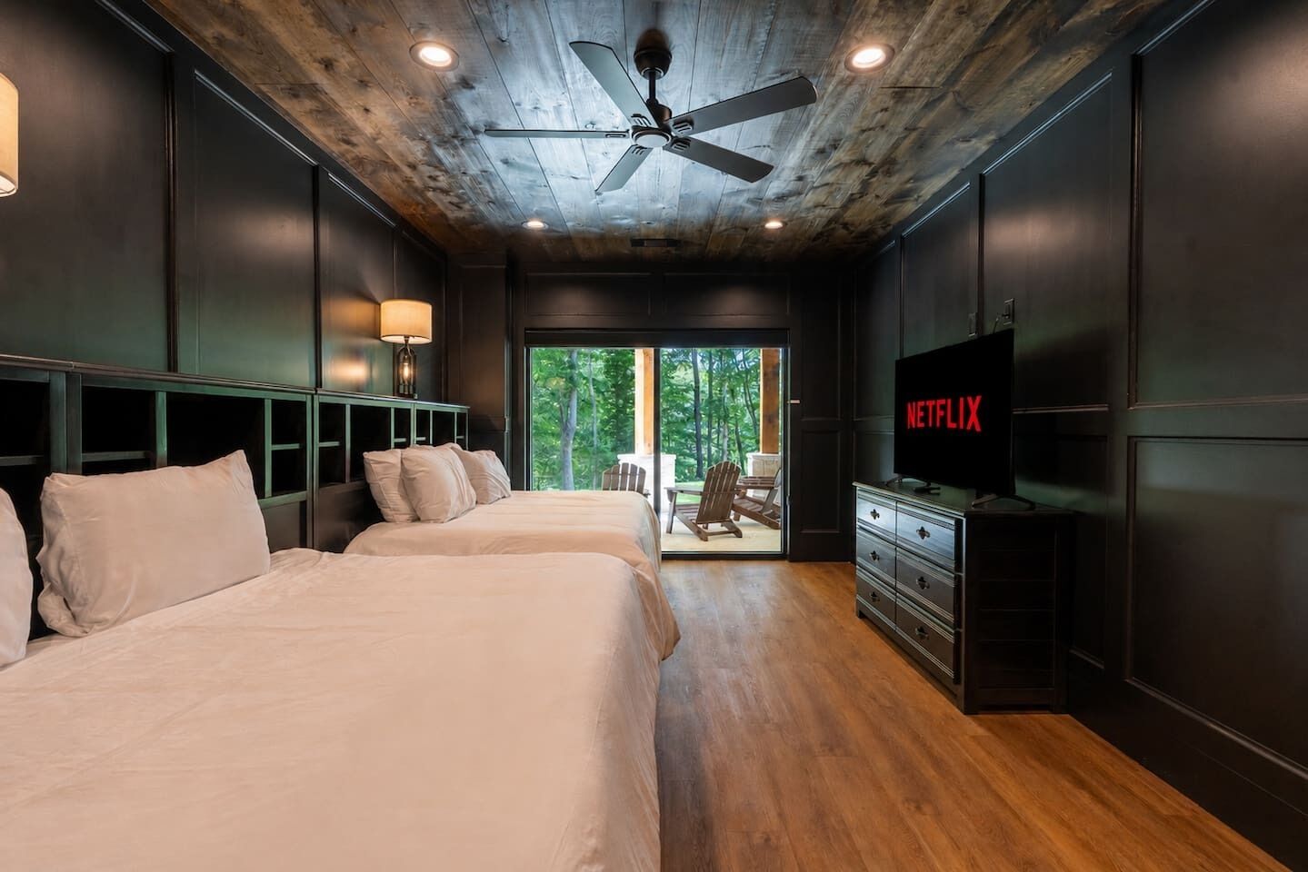 A bedroom with two beds, a ceiling fan, a TV, and a view of the outdoors.
