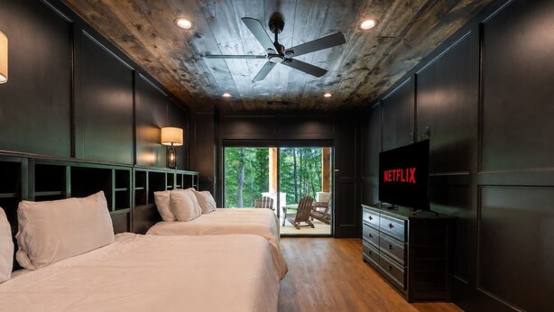 Une chambre avec deux lits, un ventilateur de plafond, une télévision et une vue sur l’extérieur.
