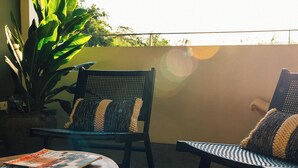 Un balcon avec deux chaises, une table avec des magazines et une grande plante.