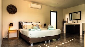 Une chambre à coucher moderne avec un grand lit, un climatiseur fixé au mur et un miroir au-dessus d’une coiffeuse.