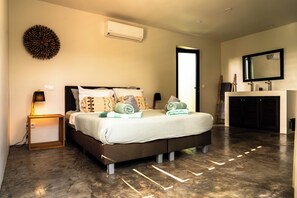 Une chambre à coucher moderne avec un grand lit, un climatiseur fixé au mur et un miroir au-dessus d’une coiffeuse.