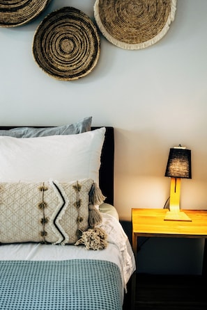 Un lit bien fait, avec une literie à motifs, une lampe de chevet et une décoration murale en fibres tressées.