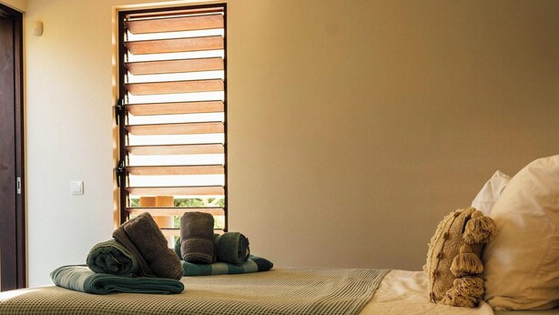 Une chambre à coucher avec un lit, des oreillers, une fenêtre avec des stores et des serviettes.