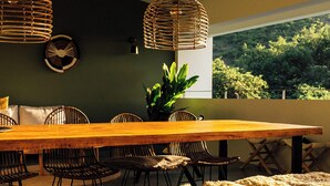 Un espace repas avec une table en bois, des suspensions en fibres tressées et une vue sur la verdure environnante.