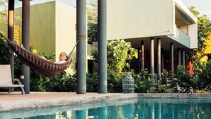 Une piscine agrémentée d’un hamac et de chaises longues, entourée de verdure et bordée d’une architecture moderne.