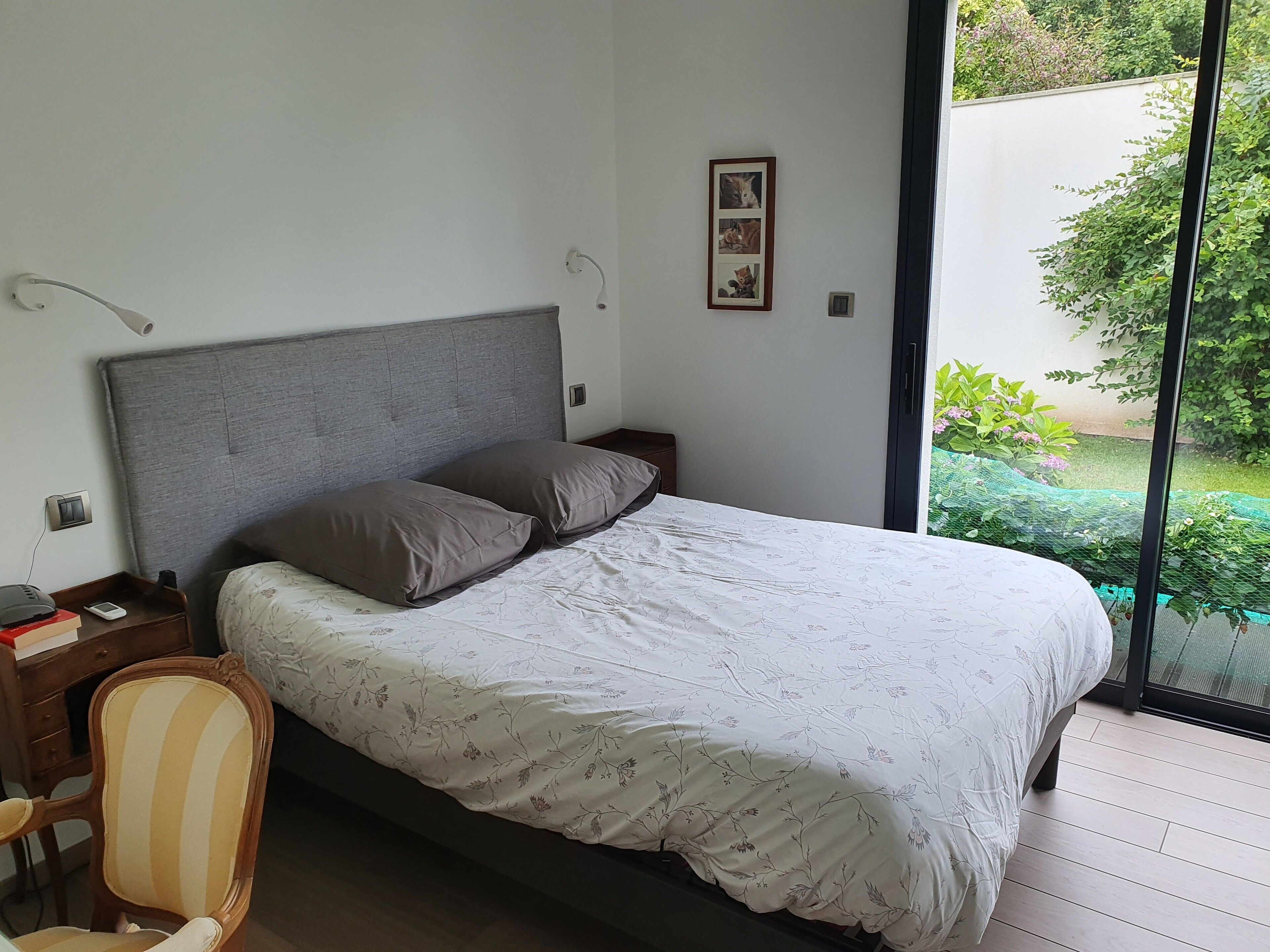A bedroom with a bed, a chair, a nightstand, and a window with a view of greenery.